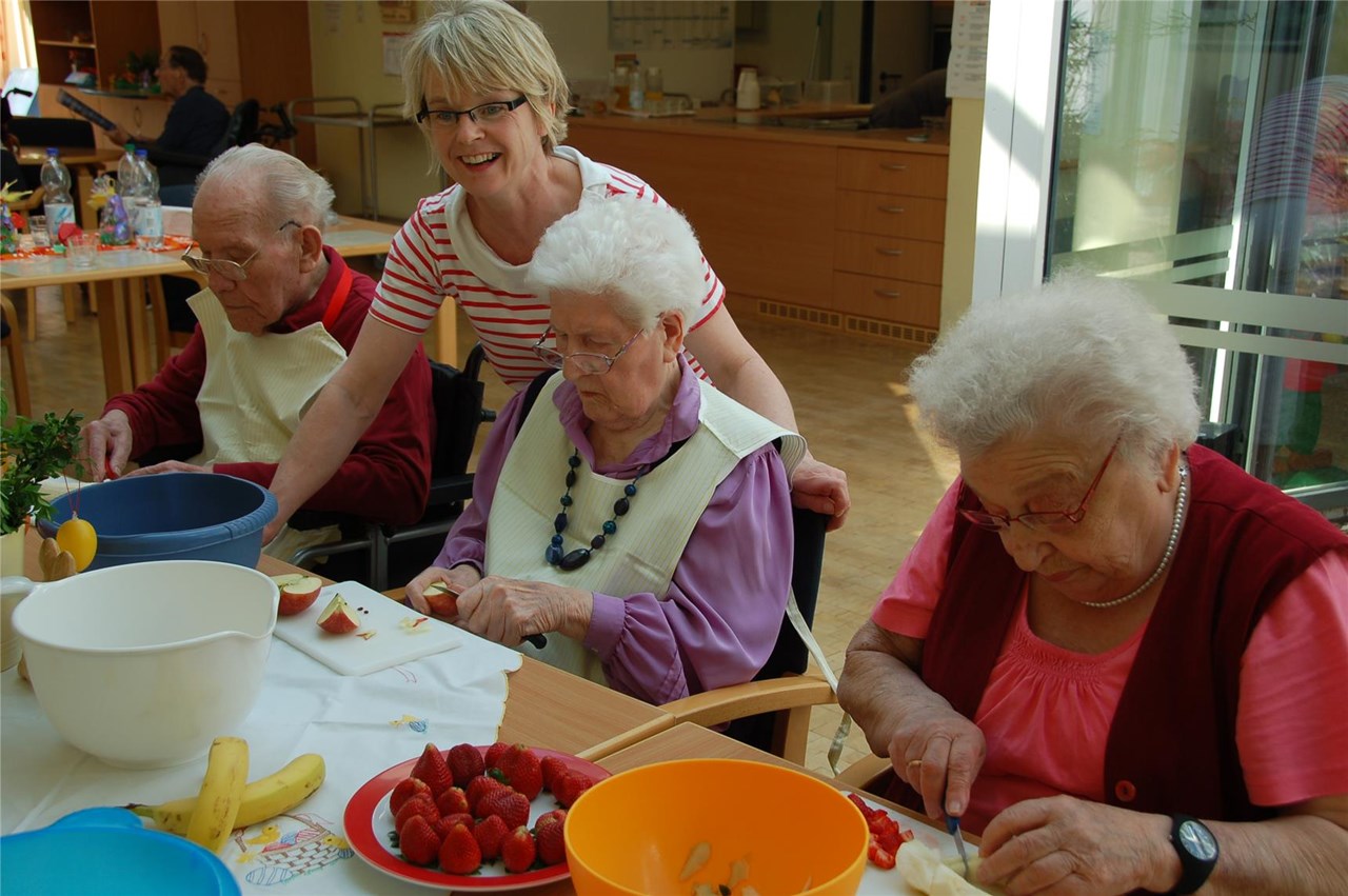 Bewohner sitzen am Tisch und schneiden Obst für den Nachtisch