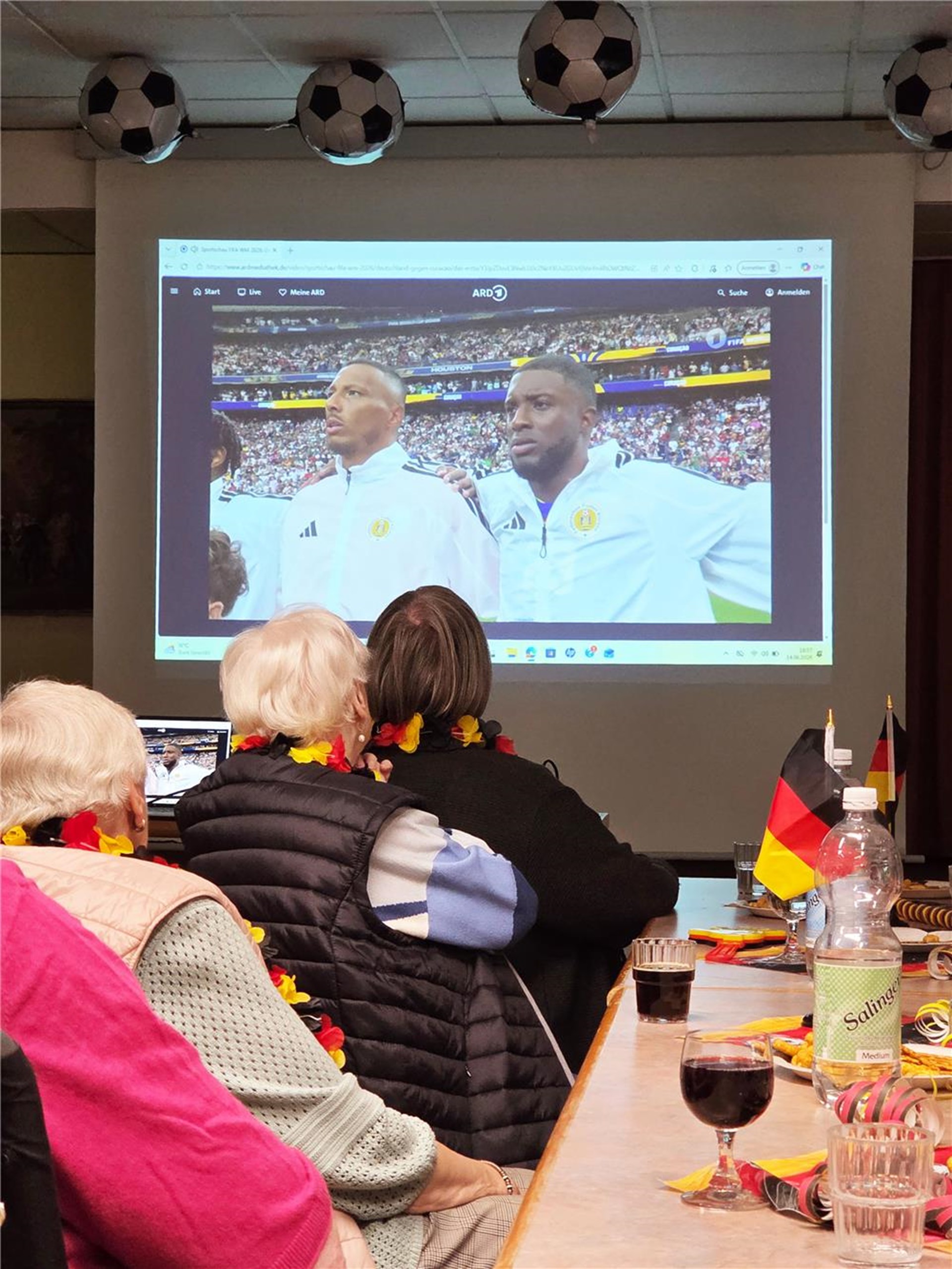 Senioren sitzen an einem langen Tisch und schauen gemeinsam Fussball