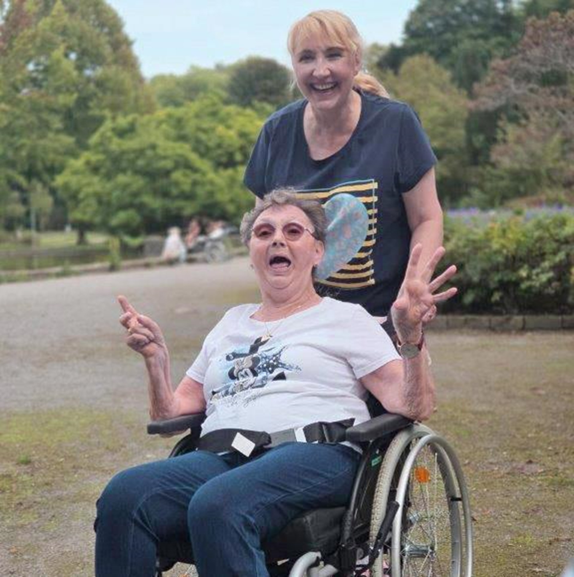 Alte Dame im Rollstuhl mit Pflegerin, beide lachen ausgelassen