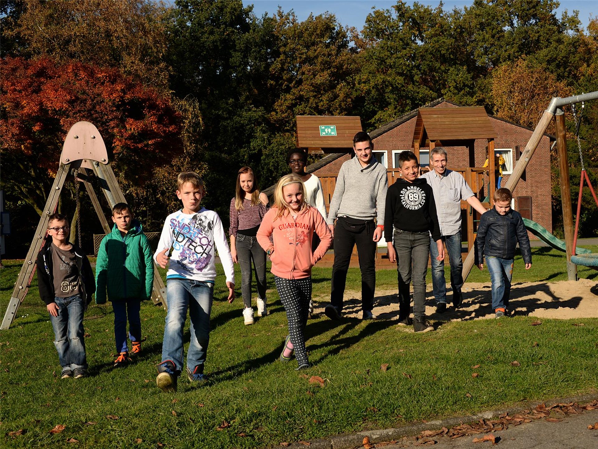 neun Kinder mit dem Heimleiter draußen auf dem Spielplatz