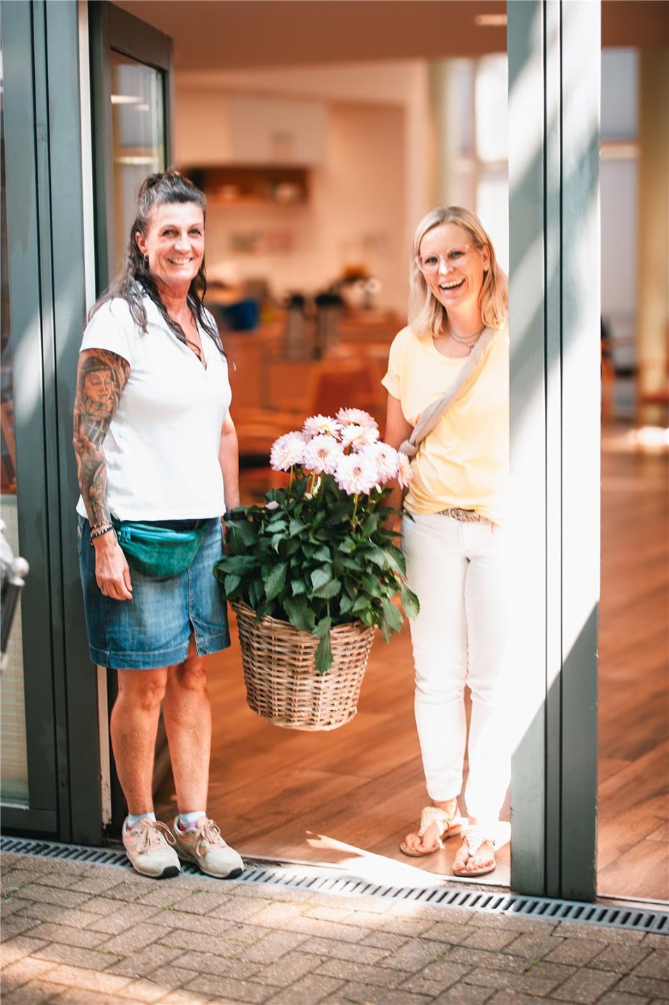 2 Mitarbeiterinnen mit Blumenkorb begrüßen die Gäste am Eingang anlässlich 25 Jahre LWH