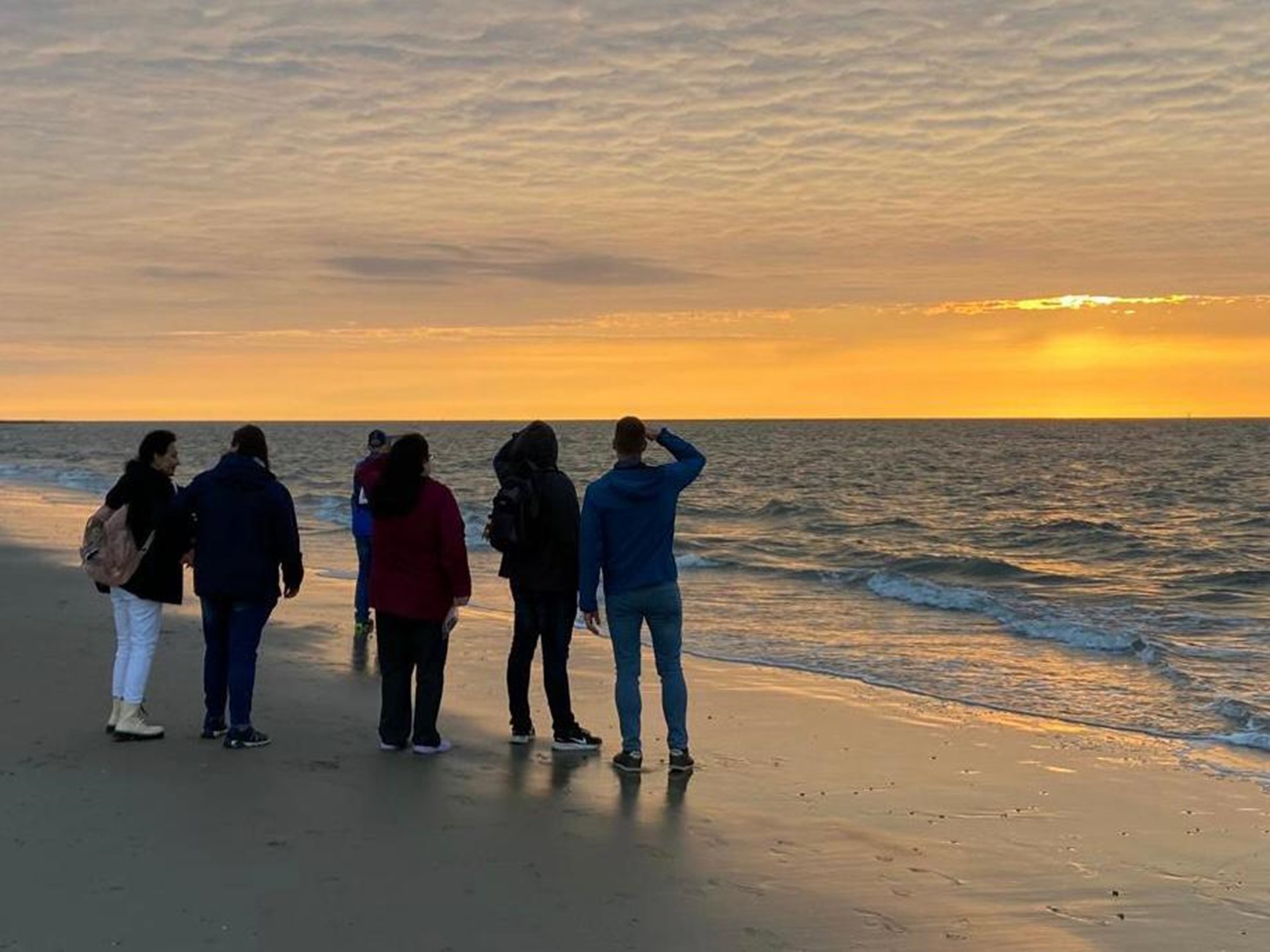 Gruppe von Menschen am Strand beobachtet Sonnenuntergang